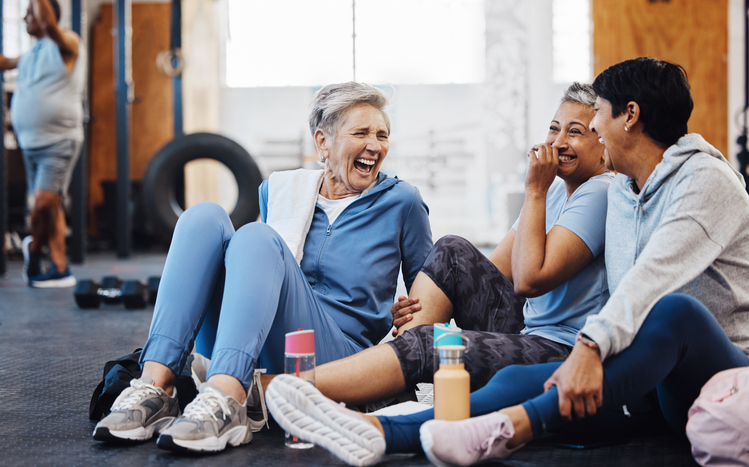 Gym, laughing and group of mature women telling joke after fitness class, conversation and comedy on floor. Exercise, bonding and happy senior woman with friends sitting chatting together at workout. stock photo