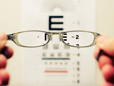 Eyeglasses in focus in front of an eye exam sheet, looking through the lenses makes the exam sheet clear.