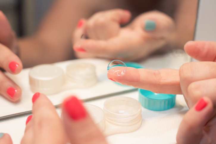 right holding a contact lens with the index finger in front of a mirror and with red painted fingernails.