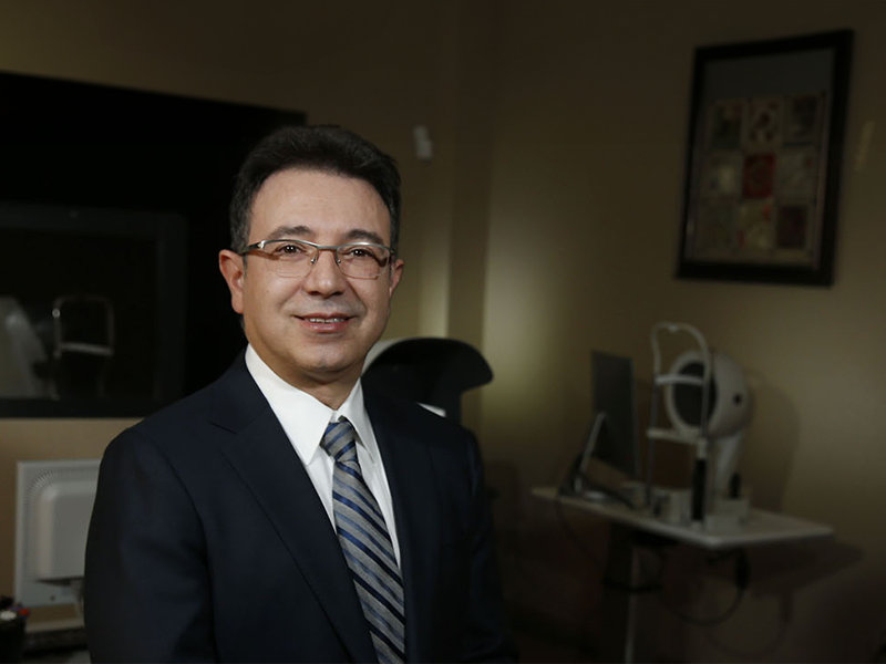 Dr. Abrams in a room at his practice with optical equipment in be background.