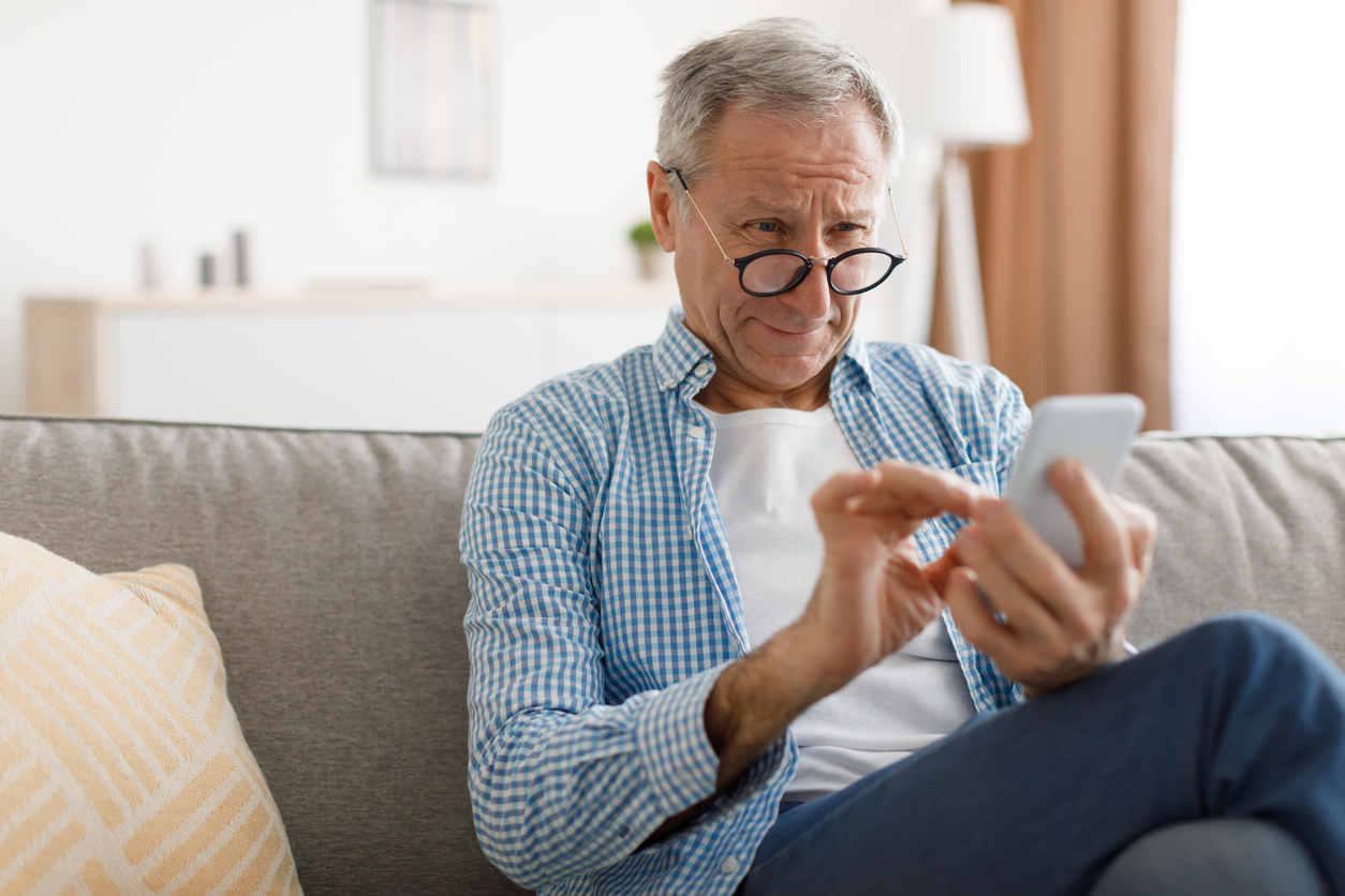 t. Senior Man Squinting Eyes Reading Message On Phone Wearing Eyeglasses Having Problems With Vision Sitting On Couch. Ophtalmic Issue, Bad Sight In Older Age, Macular Degeneration Concept